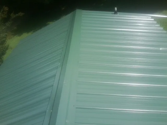 New green metal panels meeting at the ridge of a roof — Flat Roof Repair work by our crew in Harford